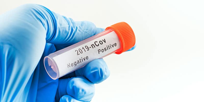 Hand with blue latex glove holding negative vial of COVID-19 test